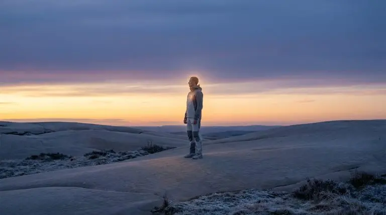 Un homme debout, éclairé par une lueur mystique au coucher du soleil dans un paysage désertique et givré.