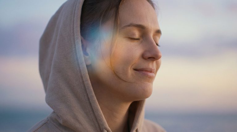 Jeune femme en sweat à capuche, les yeux fermés, avec une lumière douce et un effet de prisme autour de son oreille.